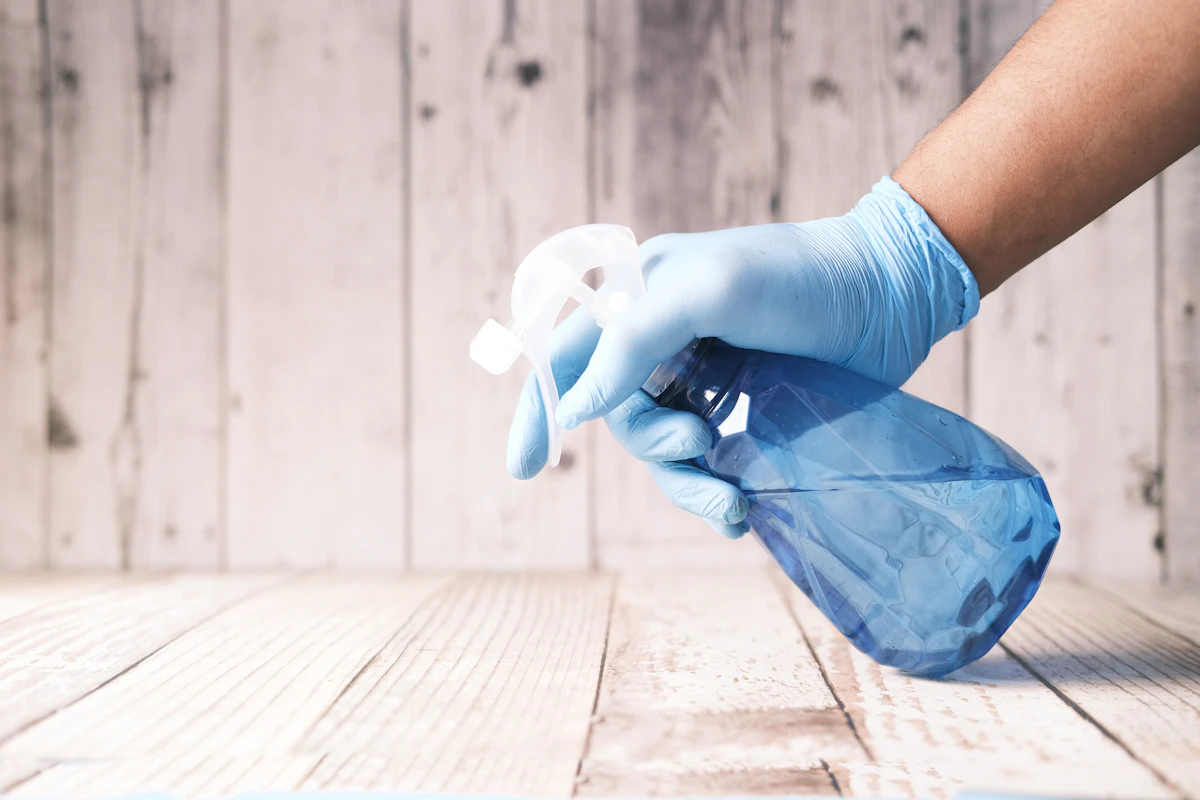 Blue-gloved hand holding a spray bottle above a wooden surface